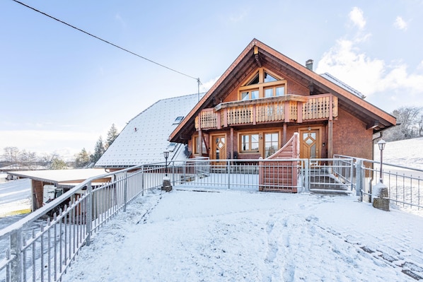 Un chalet en bois doté d’un balcon, d’un escalier menant à l’entrée et d’un sol recouvert de neige.