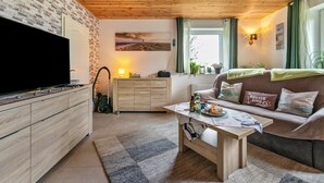 Una sala de estar con televisor, armarios de madera, un sofá, una mesa de centro y una ventana con cortinas.