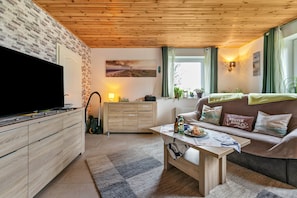 A living room with a TV, wooden cabinets, a sofa, a coffee table, and a window with curtains.