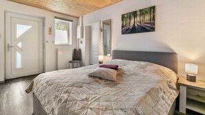 Un dormitorio con cama, ventana, puerta, espejo y un cuadro en la pared.