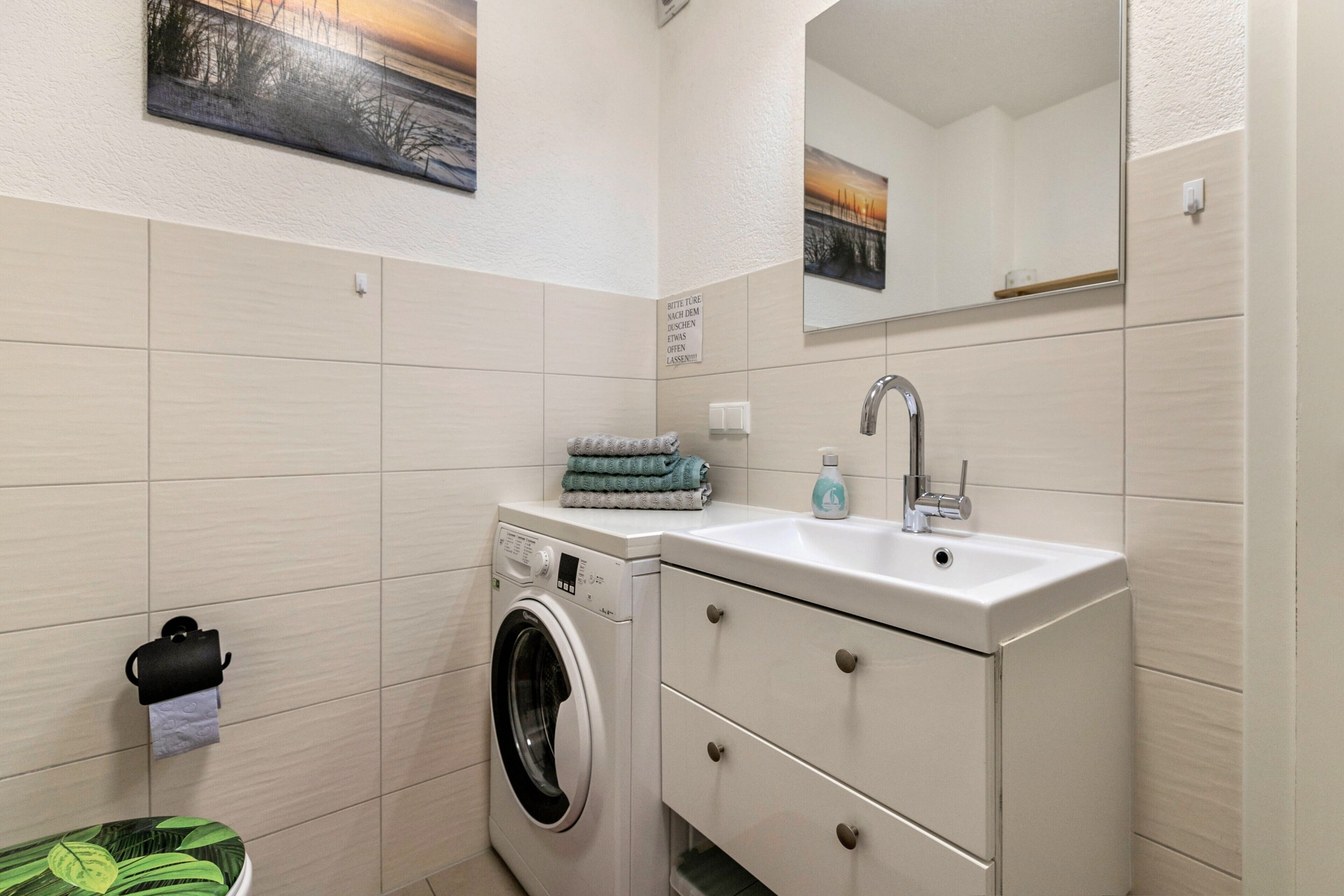 A compact bathroom with a washing machine, a sink, and a mirror.