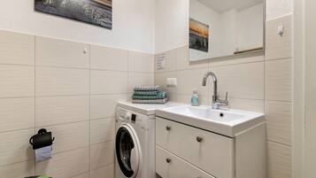 A compact bathroom with a washing machine, a sink, and a mirror.