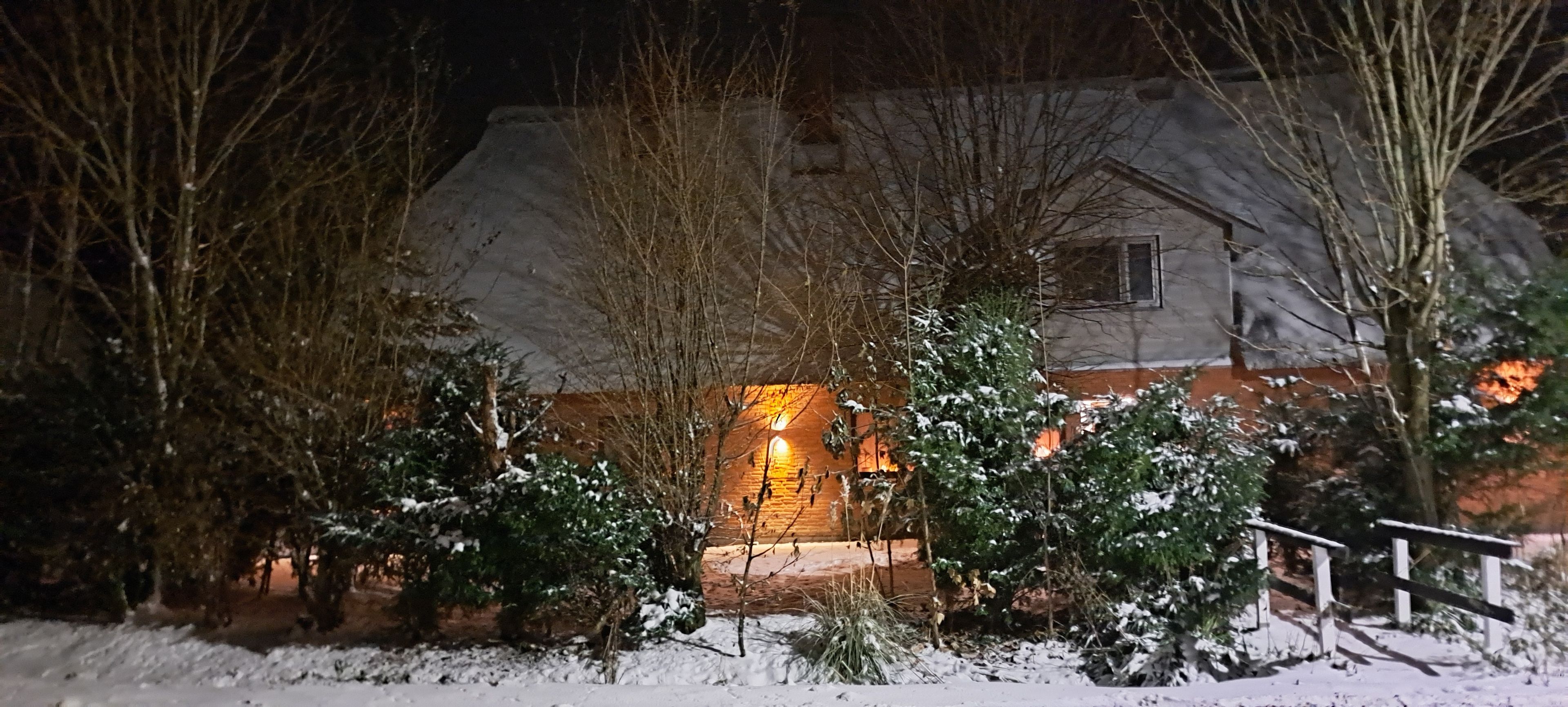 Ein Haus in einer schneebedeckten Landschaft bei Nacht, beleuchtet von warmem Innenlicht.