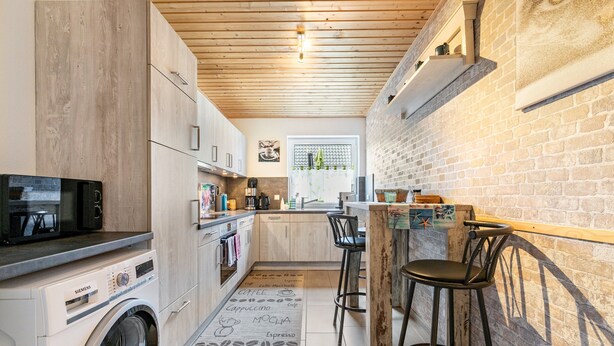 Een compacte keuken met een wasmachine, een koffieapparaat en een bar met krukken.