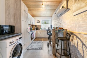 A compact kitchen with a washing machine, a coffee machine, and a bar area with stools.
