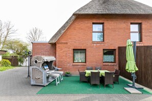 A brick house with a green lawn, outdoor furniture, and a covered table.