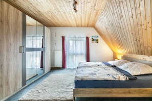 A bedroom with a wooden ceiling, a bed with patterned bedding, a large mirror, and a view of the outdoors.