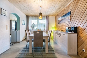 A modern kitchen with wooden cabinetry, a dining area with a table and chairs, and a view of the outdoors through a window.