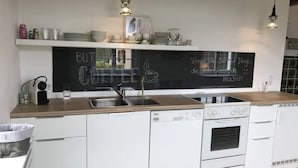 A modern kitchen with white cabinetry, a blackboard with chalk writing, and pendant lighting.