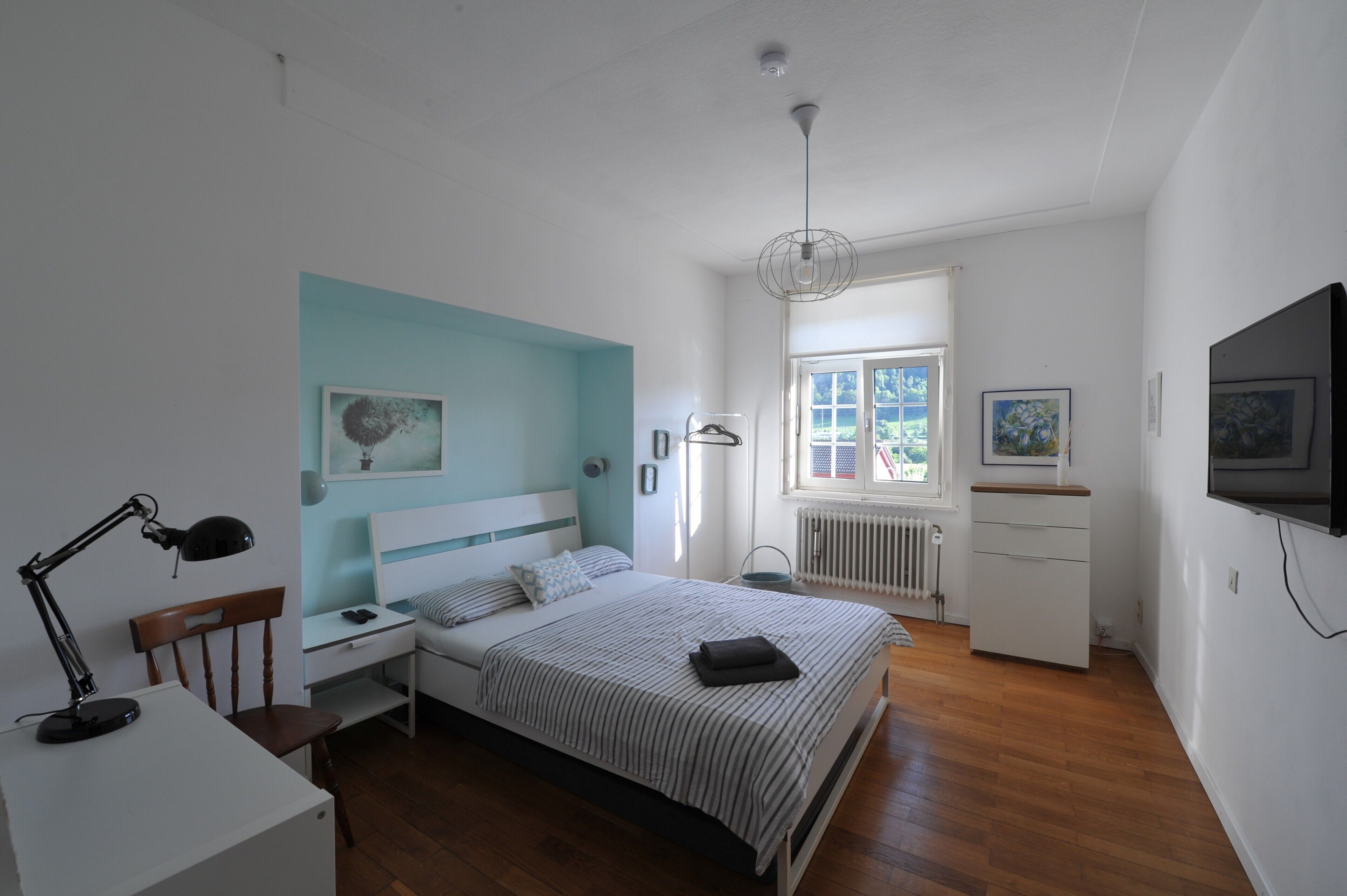 Een slaapkamer met een bed, bureau, stoel en een televisie aan de muur.