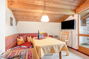 Una habitación acogedora con techo de madera, un sofá, una mesa de comedor, un televisor y una pared de piedra.