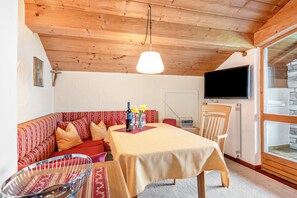 Quarto acolhedor com teto de madeira, sofá, mesa de jantar, TV e parede de pedra.