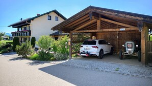 A white car parked in a covered garage with a wooden roof, a small tractor, and a sign indicating a 'Motel Trattner.' - Apartment 'Ferienwohnung Alpenblick' with Lake View, Private Garden and Wi-Fi (Waging am See-Tettenhausen)
