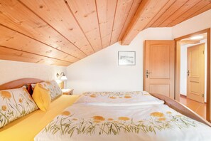 Une chambre avec un plafond en bois, un lit recouvert d’une literie à motifs floraux, une table de chevet et une porte.
