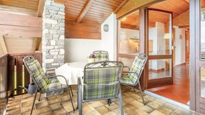 A room with a stone wall, wooden ceiling beams, a dining table with chairs, and a glass door leading to another room. - Apartment 'Ferienwohnung Alpenblick' with Lake View, Private Garden and Wi-Fi (Waging am See-Tettenhausen)