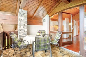 Une pièce avec un mur en pierre, des poutres en bois au plafond, une table à manger avec des chaises et une porte en verre donnant sur une autre pièce.