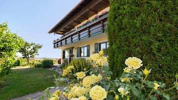 Un immeuble doté d’un balcon, entouré d’un jardin bien entretenu où poussent des rosiers jaunes.