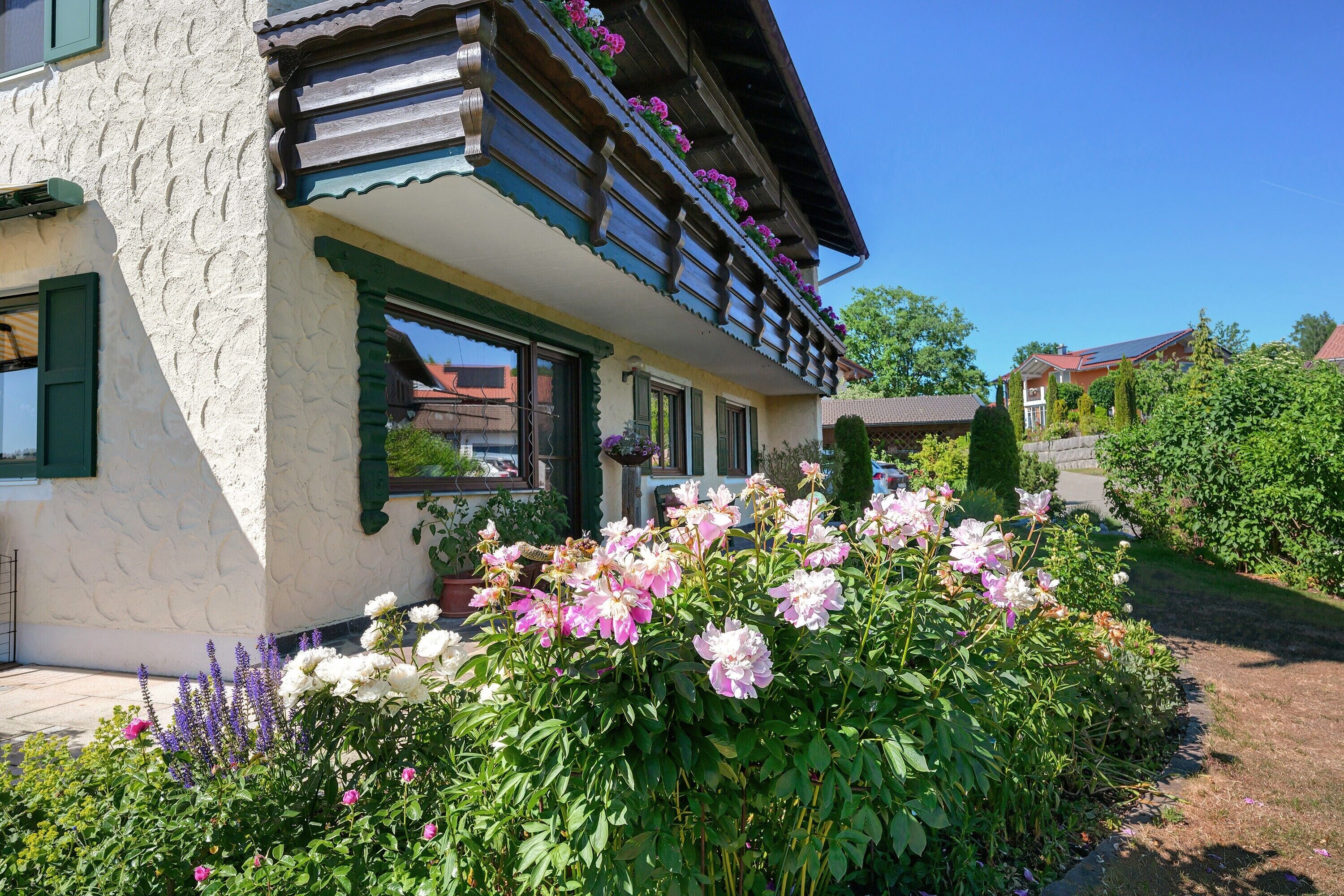 Ein traditionelles Gebäude mit Balkon, umgeben von einem Garten mit verschiedenen Blumen.