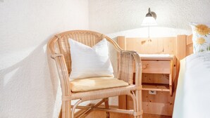 Una silla de mimbre con cojín, un escritorio de madera y una lámpara fijada a la pared.