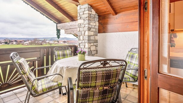A covered patio with a stone fireplace, outdoor seating, and a view of the landscape.