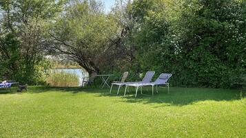 Ein grasbewachsener Außenbereich mit Tisch und Stühlen, umgeben von dichtem Grün und Bäumen.