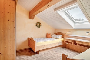 Quarto com cama de madeira, escrivaninha, claraboia e luminária na parede.