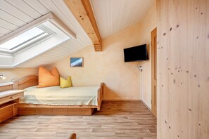 A bedroom with a sloped ceiling, wooden floor, a bed with pillows, a TV mounted on the wall, and a small picture.