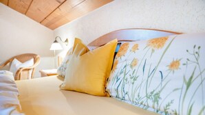 A bed with floral bedding, a yellow pillow, and a headboard with a floral pattern. - Apartment 'Ferienwohnung Alpenblick' with Lake View, Private Garden and Wi-Fi (Waging am See-Tettenhausen)