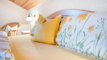 Una cama con ropa de cama floral, un cojín amarillo y un cabecero con estampado de flores.