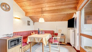 Una habitación acogedora con techo de madera, una mesa de comedor con sillas, un sofá, una pequeña cocina con estufa y un televisor.