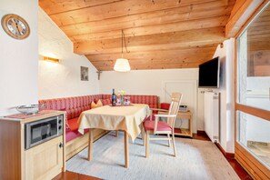 Una habitación acogedora con techo de madera, una mesa de comedor con sillas, un sofá, una pequeña cocina con estufa y un televisor.
