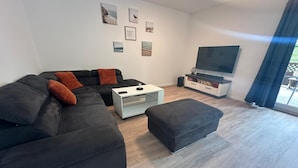 Un salon moderne avec un canapé d’angle, une table basse, un téléviseur à écran plat et des œuvres d’art accrochées au mur.