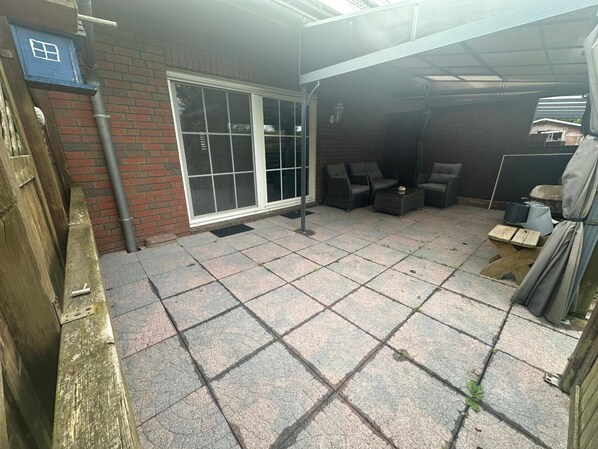 A patio area with a tiled floor, a sliding glass door, outdoor furniture, and a brick wall.