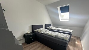 Une chambre à coucher avec un lit, des tables de chevet, une fenêtre et un radiateur.