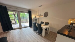Une pièce spacieuse comprenant une table à manger, des chaises, une horloge et une fenêtre avec des rideaux.