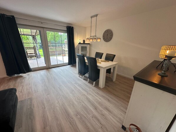 A spacious room with a dining table, chairs, a clock, and a window with curtains.