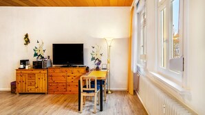 Una habitación con techo de madera, televisor, aparador, mesa, silla, lámpara de pie y ventana.