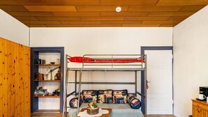 Una cama litera con una cama inferior, una mesita con una planta y una estantería con libros y objetos decorativos.