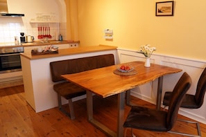 Une cuisine avec des plans de travail en bois, un banc intégré, une table à manger avec des chaises et un vase de fleurs posé sur la table.