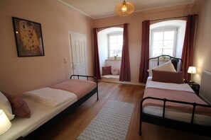 Une chambre avec deux lits simples, une fenêtre avec des rideaux, un tableau au mur et un luminaire au plafond.