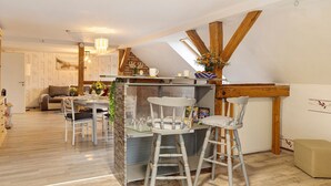 Une cuisine moderne avec un coin repas, des poutres en bois et une chambre à coucher située en mezzanine.