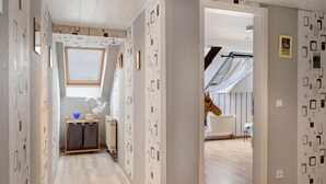 Un couloir aux murs ornés de motifs, avec une lucarne, un radiateur et un plancher en bois.
