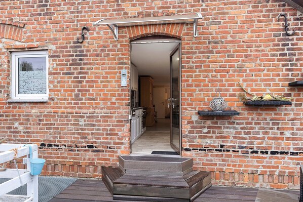 A brick building with a wooden deck, a door leading to a hallway, and a small shelf with a decorative item.