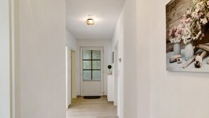 A hallway with a wooden floor, a white door, and a framed floral arrangement on the wall.