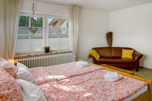 Une chambre à coucher avec un lit, une fenêtre avec des rideaux, un radiateur, un canapé en cuir marron et une plante en pot.