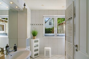 Une salle de bain équipée d’un lavabo, d’un miroir, d’un porte-serviettes et d’une fenêtre donnant sur un espace verdoyant.