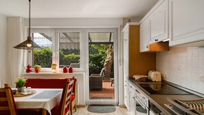 A kitchen with a dining area, a view to the outside, and a large tree visible through the glass door.