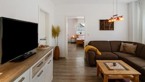 A living room with a flat-screen TV, a wooden coffee table, a brown sofa, and a hanging light fixture.