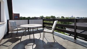 A balcony with a round table and two chairs, a wooden fence, and a view of buildings and trees.