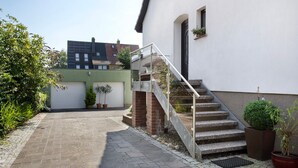 A residential building with a staircase leading to a garage, a paved driveway, and potted plants.